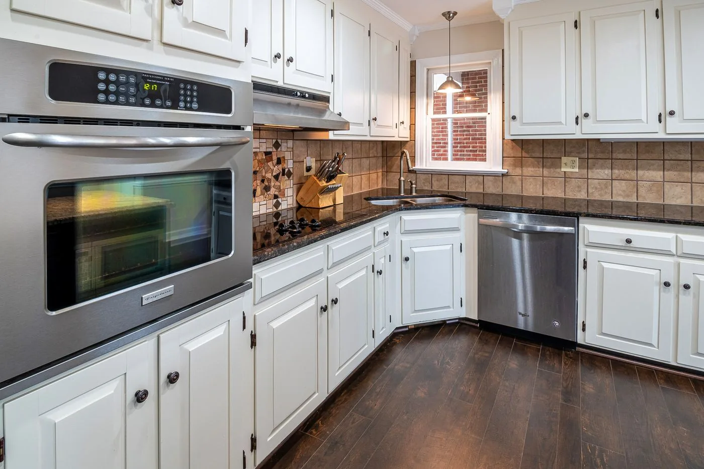 A kitchen of white cabinets with stainless appliances and wood flooring