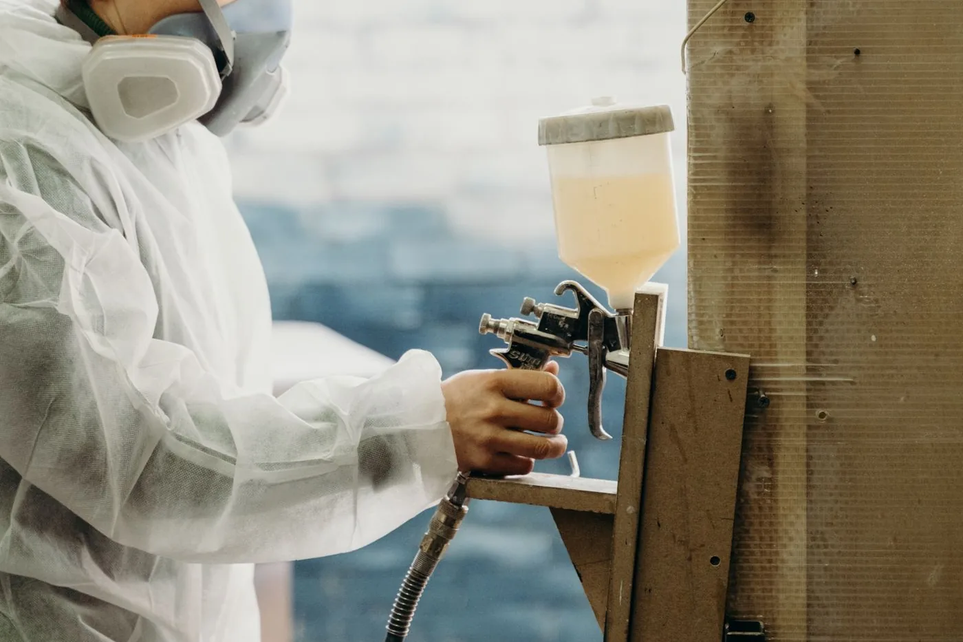 A finisher in protective gear spraying a workpiece in a workshop booth