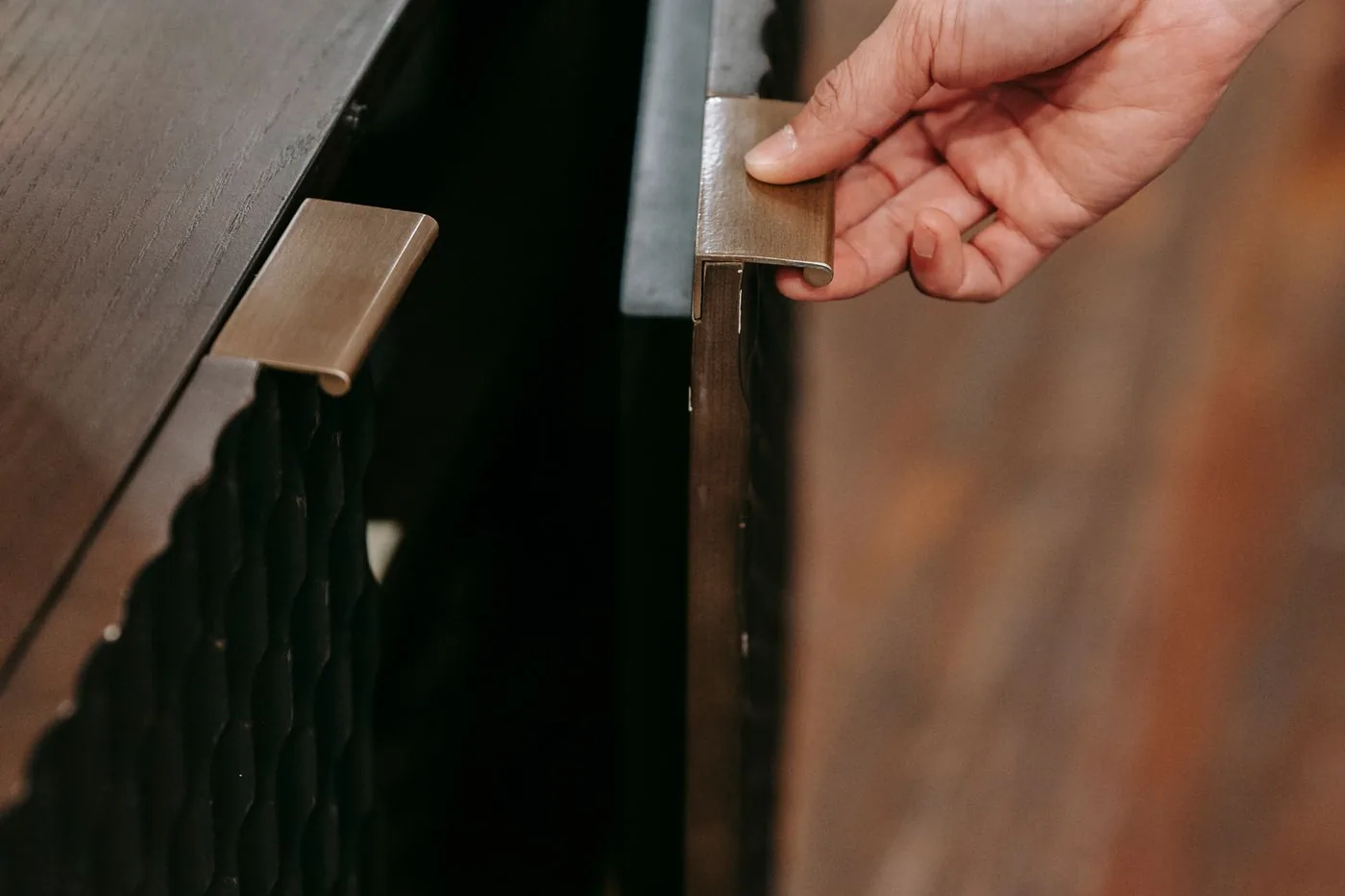 A hand opening the door of a wooden kitchen cabinet